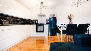 A modern kitchen with white cabinets, a black refrigerator, and a dining area with a table and chairs. - LUX Woolwich Flat 2 Stops to Canary Wharf (London)