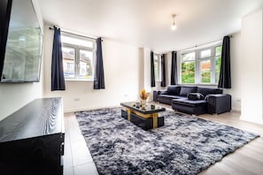 A modern living room with a black sofa, a coffee table, and a TV on a stand. - LUX 2bdr Flat Near LTN Airport City Centre (Luton)
