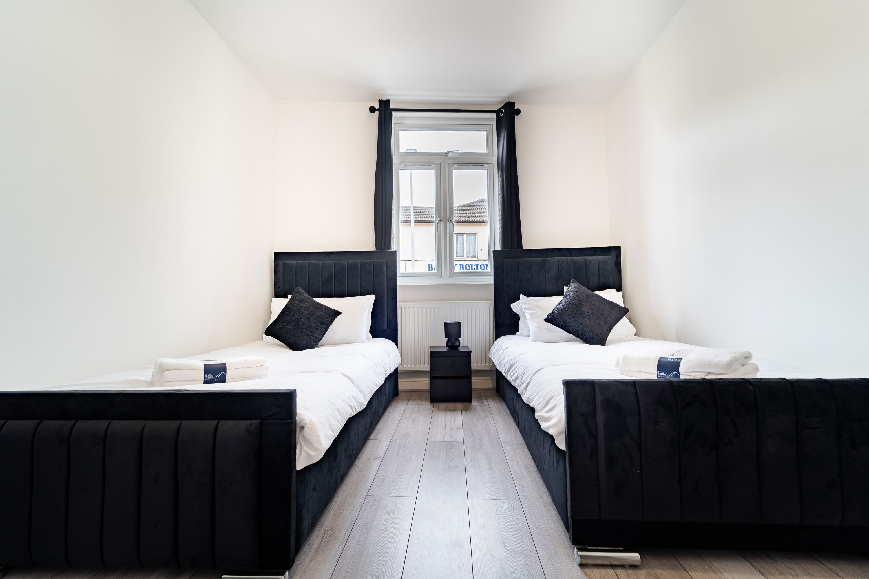 Een tweepersoonskamer met twee bedden, een klein nachtkastje, een raam met gordijnen en een radiator.