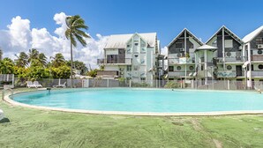 Un complejo turístico con piscina, edificios de varios pisos y un área cercada con sillones de descanso.