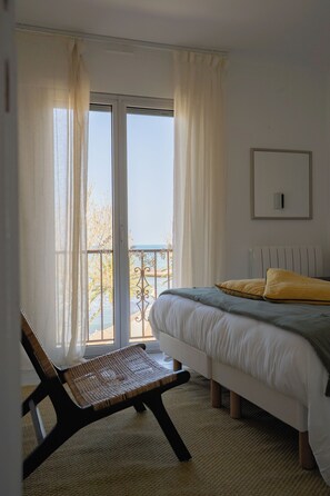 A bedroom with a bed, a chair, a view through a window, and a balcony. - Cozy, bright duplex with an ocean view   (Collioure)