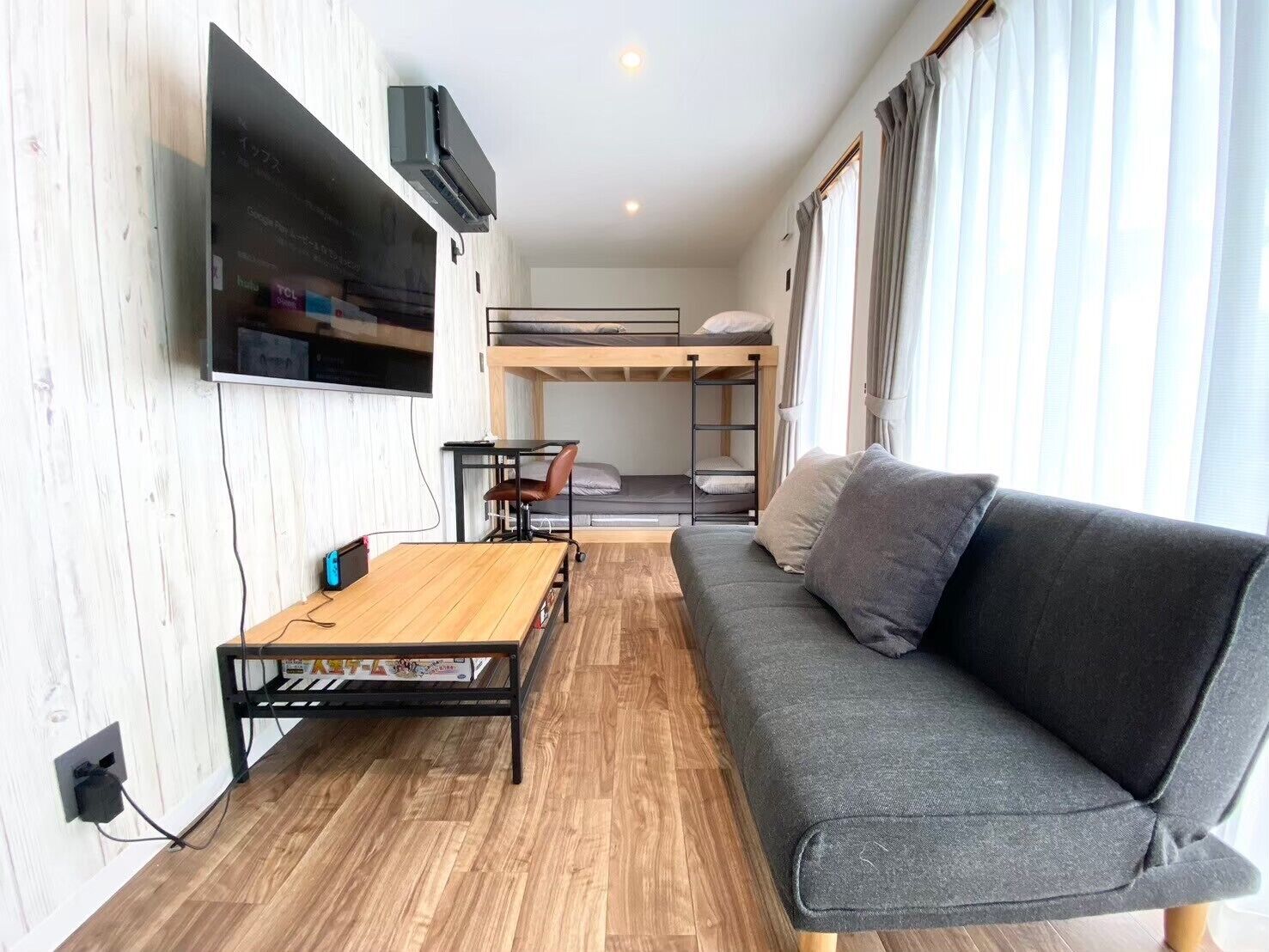 Una stanza con un letto a castello, un divano, una TV appesa al muro e un piccolo tavolo.