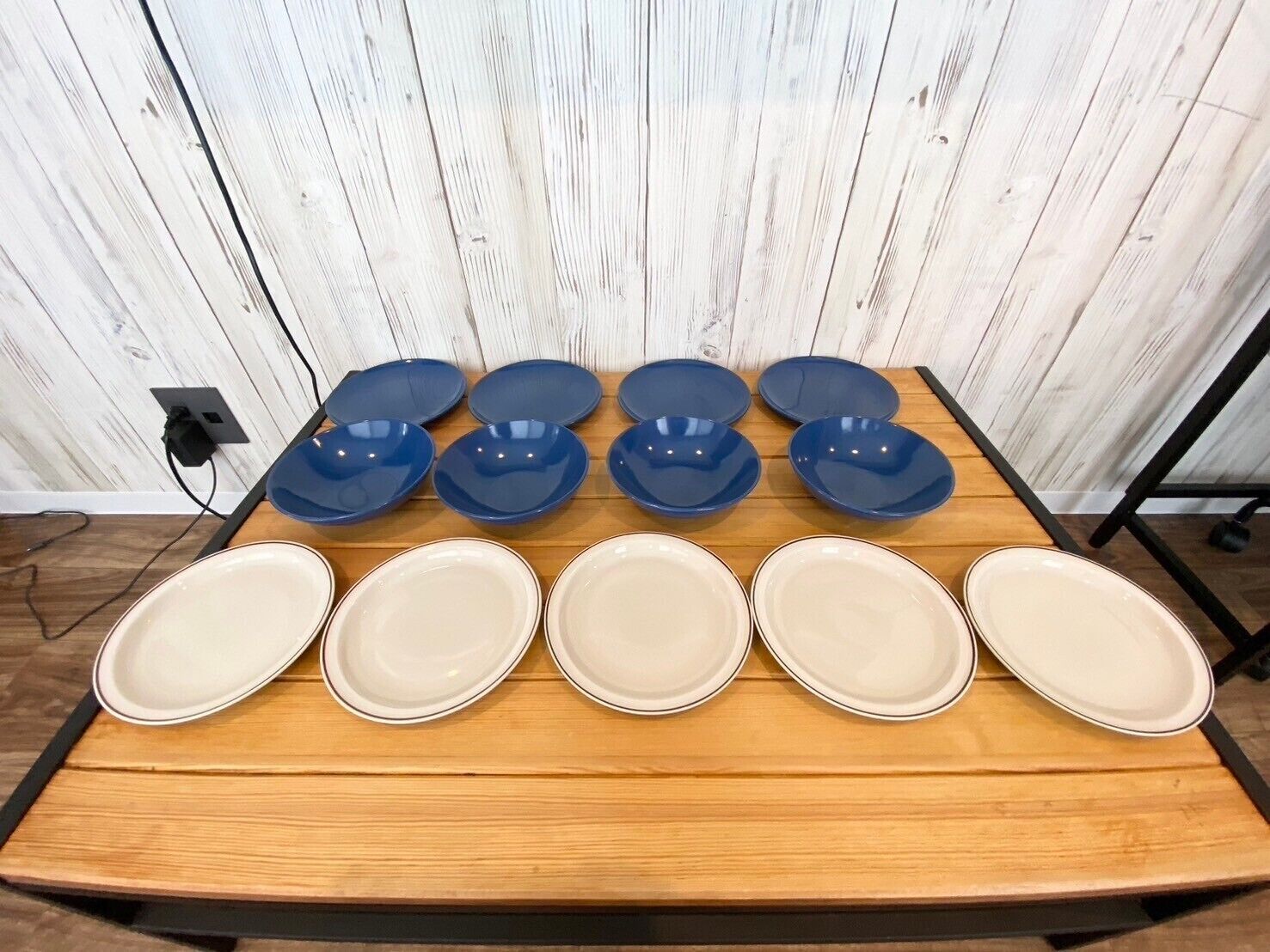 A table with eight plates, six blue and two white, against a wooden wall with a power outlet.