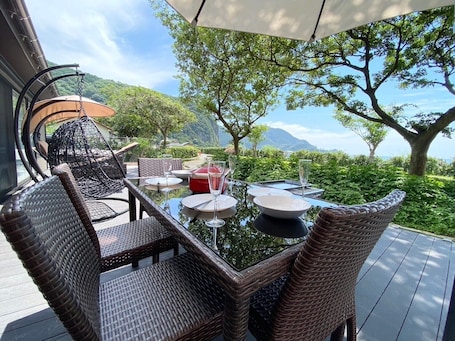 An outdoor dining area with wicker furniture, a glass table, and a view of the landscape.