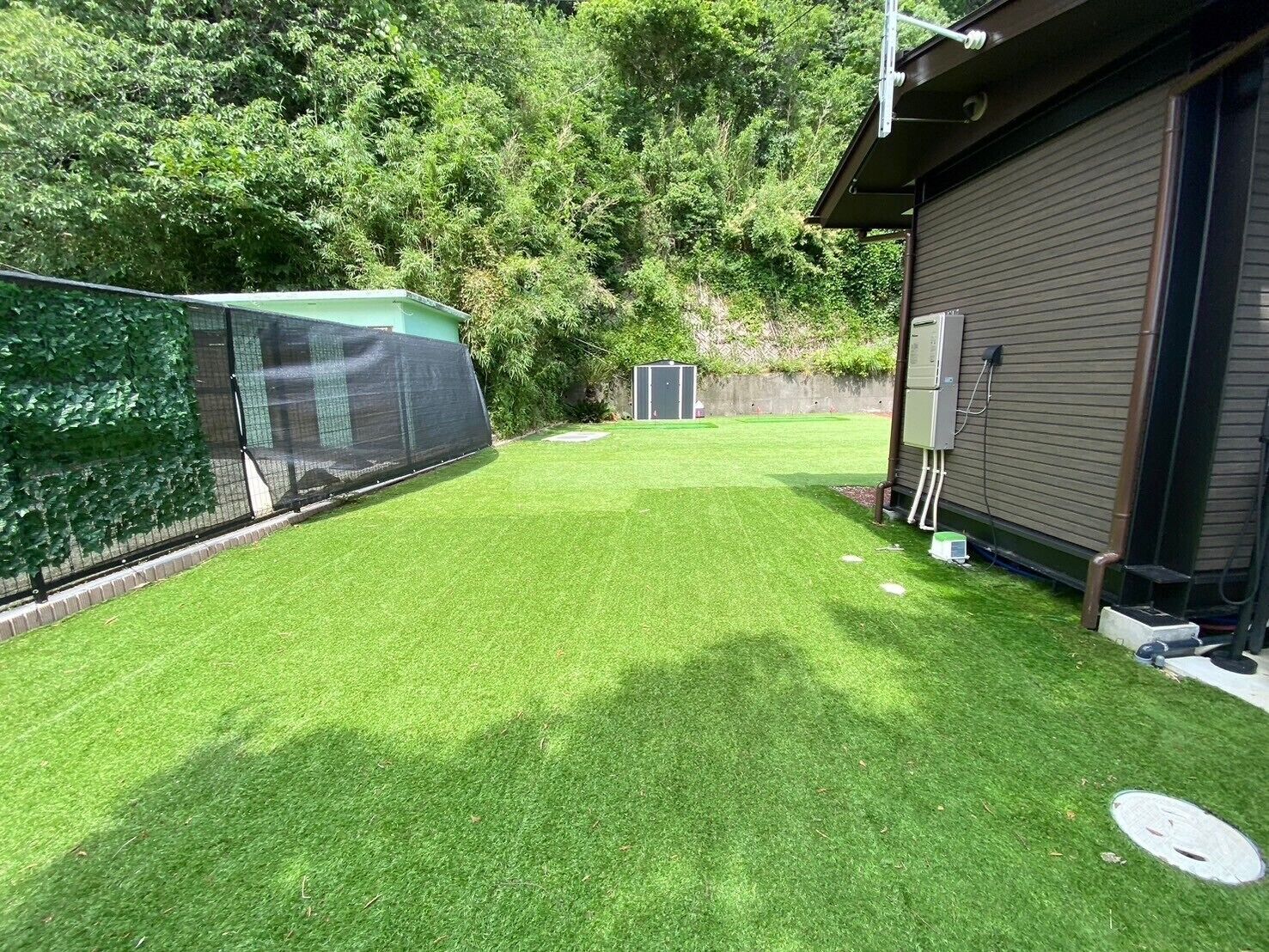 Een achtertuin met kunstgras, een omheind gebied, een tuinhuis en een gebouw met een bruine gevel.