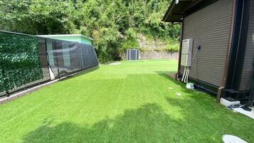 Een achtertuin met kunstgras, een omheind gebied, een tuinhuis en een gebouw met een bruine gevel.