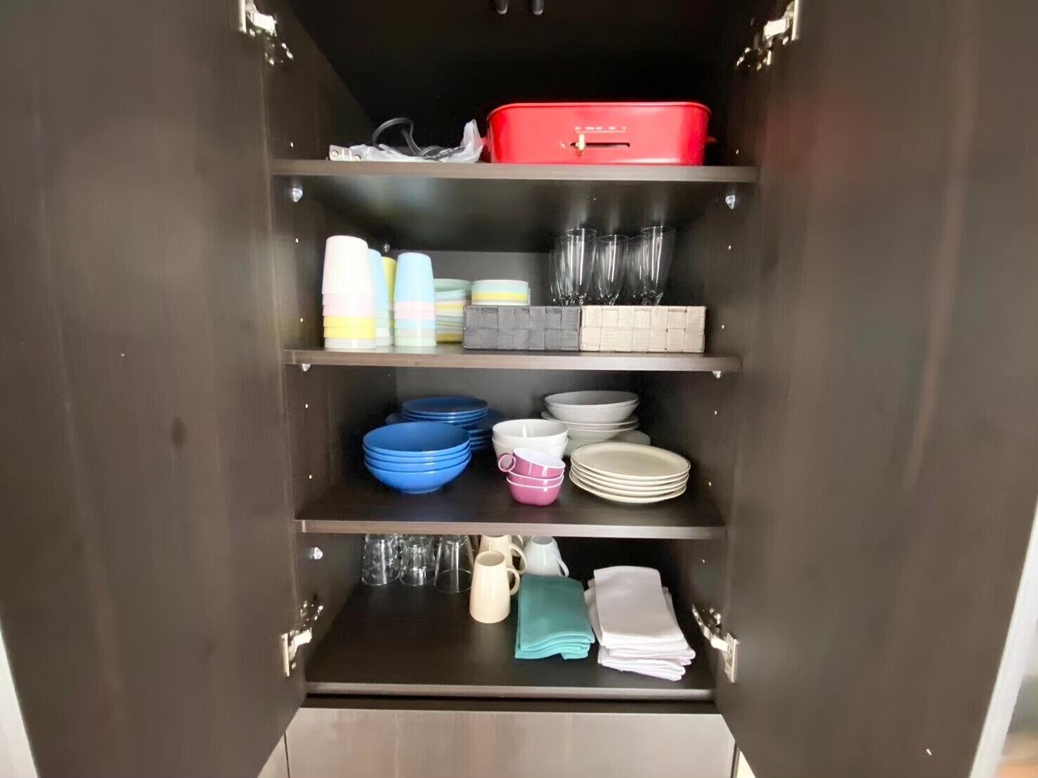 Un compartimento con estantes que contiene diverso menaje de cocina, incluyendo platos, tazones y tazas.