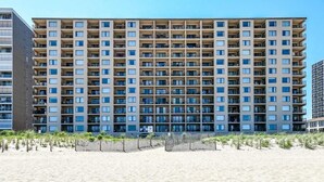 Ein mehrstöckiges Hotel mit einheitlicher Fassade, Balkonen und einem Sandstrand im Vordergrund.