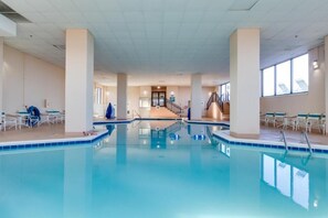 A large indoor swimming pool with clear water, surrounded by white walls and columns, with a staircase leading to an upper level. - Oceanfront 3 bedroom corner condo with panormaic ocean, indoor pool and bay views! MB701 (Ocean City)