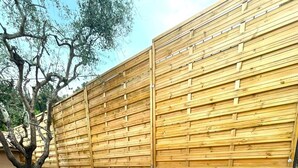 Eine Terrasse mit einem runden Tisch und zwei Stühlen, einer Steinmauer und einem Holenzaun.