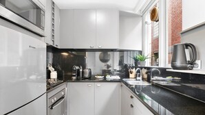 A modern kitchen with white cabinets, a black countertop, stainless steel appliances, and a window with a view of a brick building. - St Kilda Retreat Near Beach & Cafes (Melbourne)
