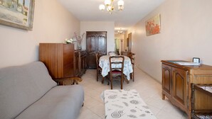 Ein Zimmer mit einer Couch, einem Esstisch mit Stühlen, einer Holzkommode und einem Kronleuchter.