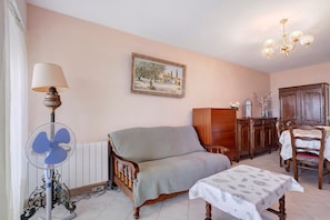 A living room with a sofa, a table, a fan, a radiator, a wooden cabinet, and a chandelier. - Holiday Home 'Appart - Piscine Et Vue Sur Le Port' with Sea View, Shared Pool and Wi-Fi (Menton)
