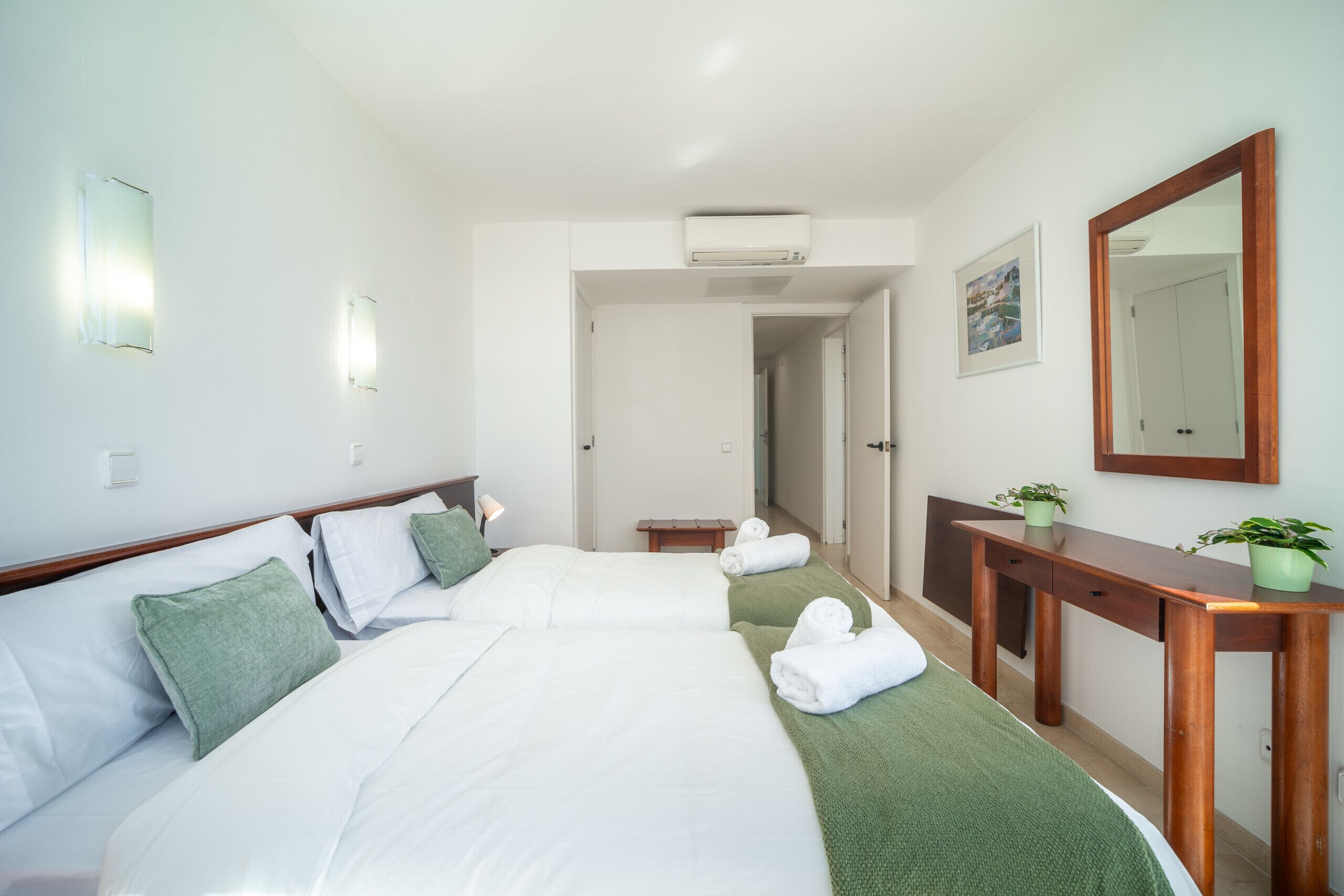 A hotel room with two beds, a wooden desk, a mirror, and a framed picture on the wall.