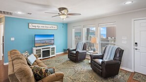 A living room with a television, two leather chairs, a sofa, and a ceiling fan. - Crystal Blue - 2nd Row - Easy Beach access, fenced yard, steps to the beach! (Crystal Beach)