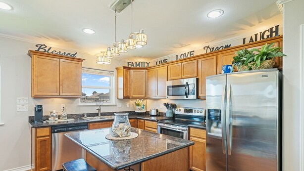A kitchen with wooden cabinets, stainless steel appliances, a granite countertop, and a central island with stools. - Crystal Blue - 2nd Row - Easy Beach access, fenced yard, steps to the beach! (Crystal Beach)