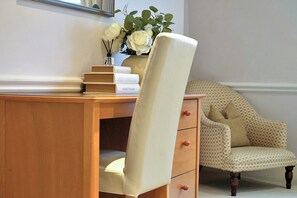 A wooden desk with a white chair, a vase with white flowers, and a stack of books. - Hertford Flat 14 (London)