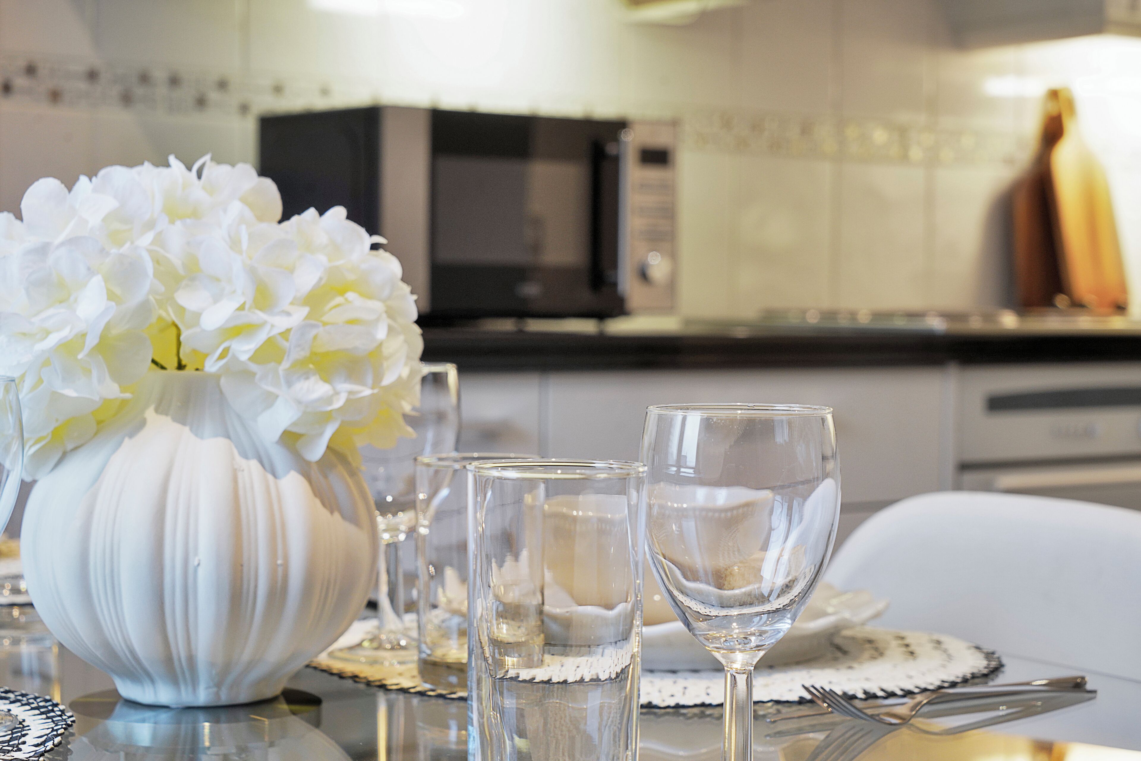 Een eettafel met een witte vaas, glazen en een bord met bestek.
