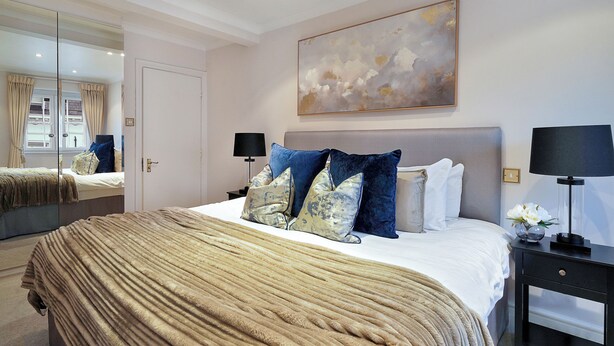 A bedroom with a large bed, two bedside tables, a mirror, and a painting on the wall. - Hertford Flat 14 (London)