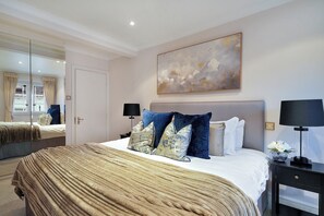 Ein Schlafzimmer mit einem großen Bett, zwei Nachttischen, einem Spiegel und einem Bild an der Wand.