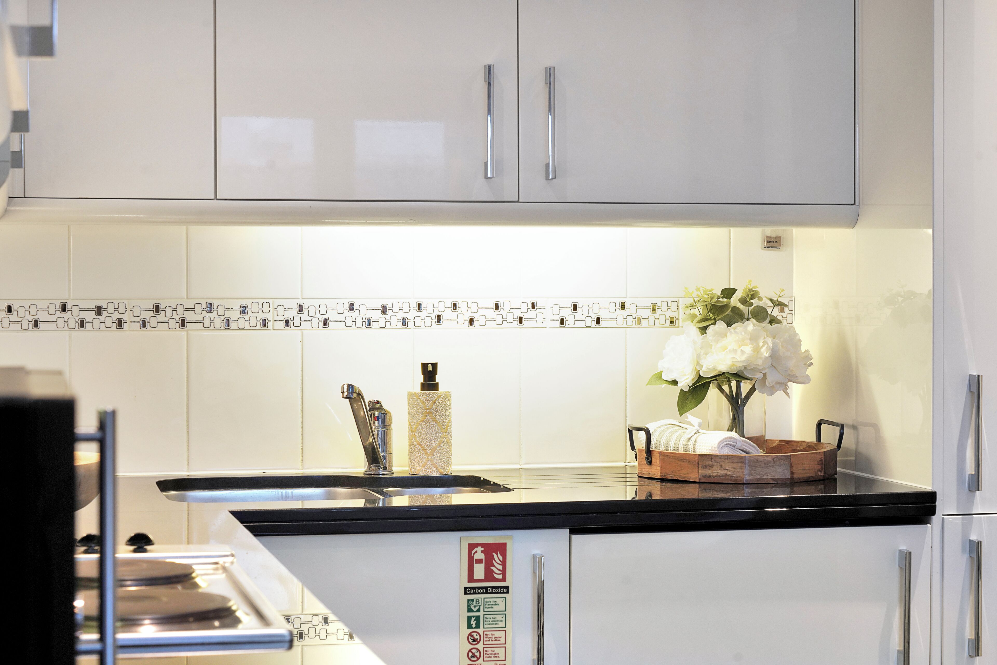 A kitchen with white cabinets, a black countertop, a stainless steel sink, a fire extinguisher, and a sign about carbon dioxide.