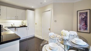 A modern kitchen with white cabinets, a dining area with a glass table set for four, and a framed artwork on the wall. - Hertford Flat 14 (London)