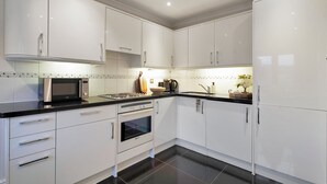 A modern kitchen with white cabinets, stainless steel appliances, and a black countertop. - Hertford Flat 14 (London)