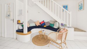 Un intérieur moderne avec un escalier blanc, un canapé incurvé agrémenté de coussins colorés, un fauteuil en osier et une petite table ronde.