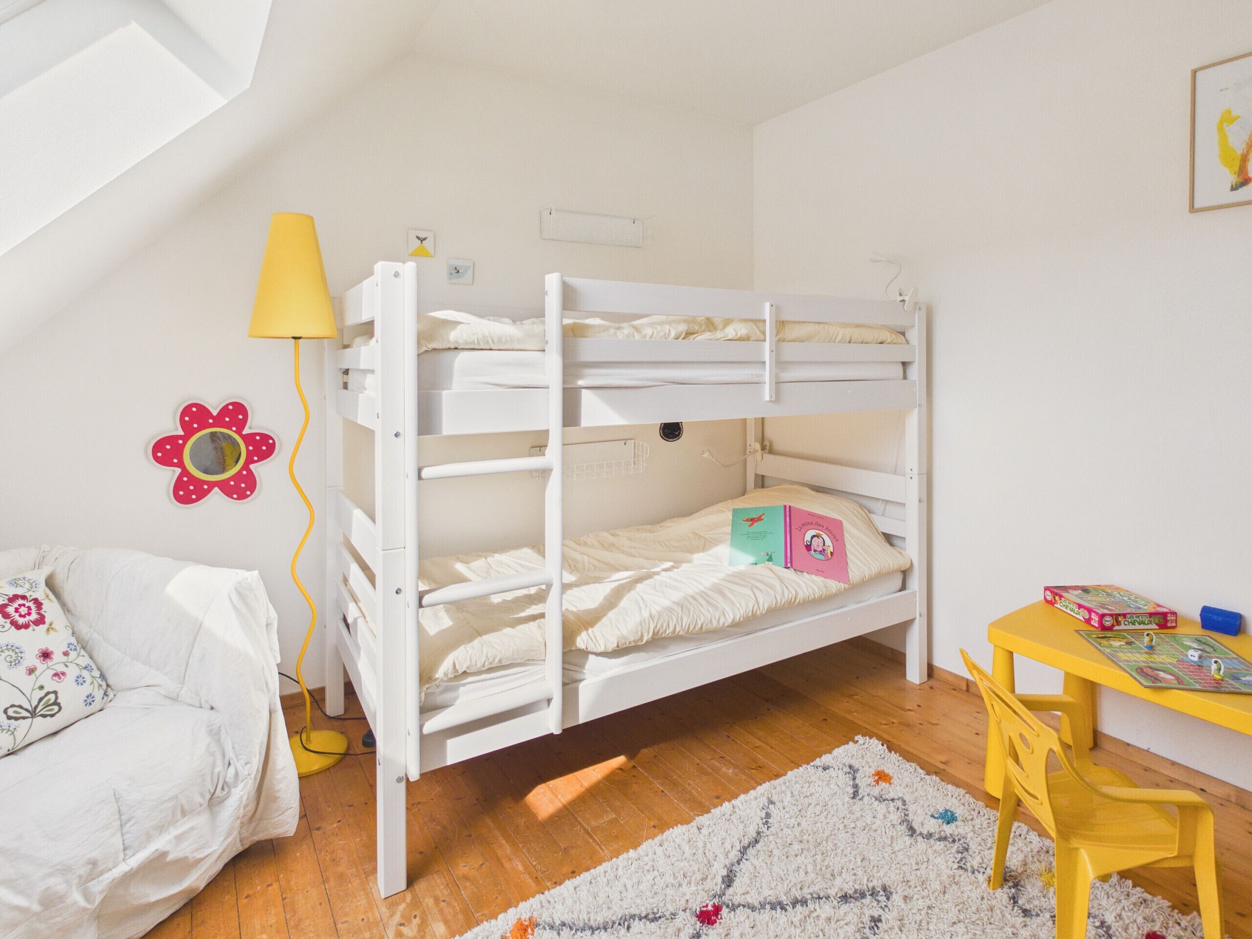 A bunk bed room with a desk, a lamp, and a flower decoration on the wall.