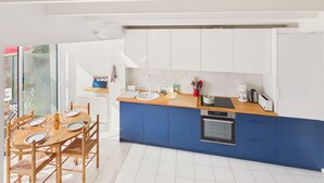 Une cuisine moderne avec des meubles blancs et bleus, une table à manger en bois avec des chaises et un four encastré.