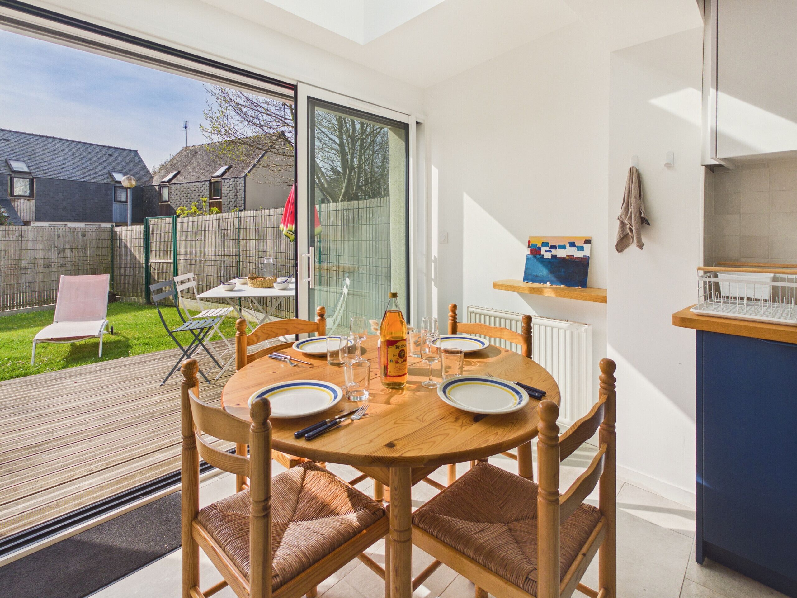 A dining area with a table set for four, a kitchen area with a blue countertop, and a view of a backyard.