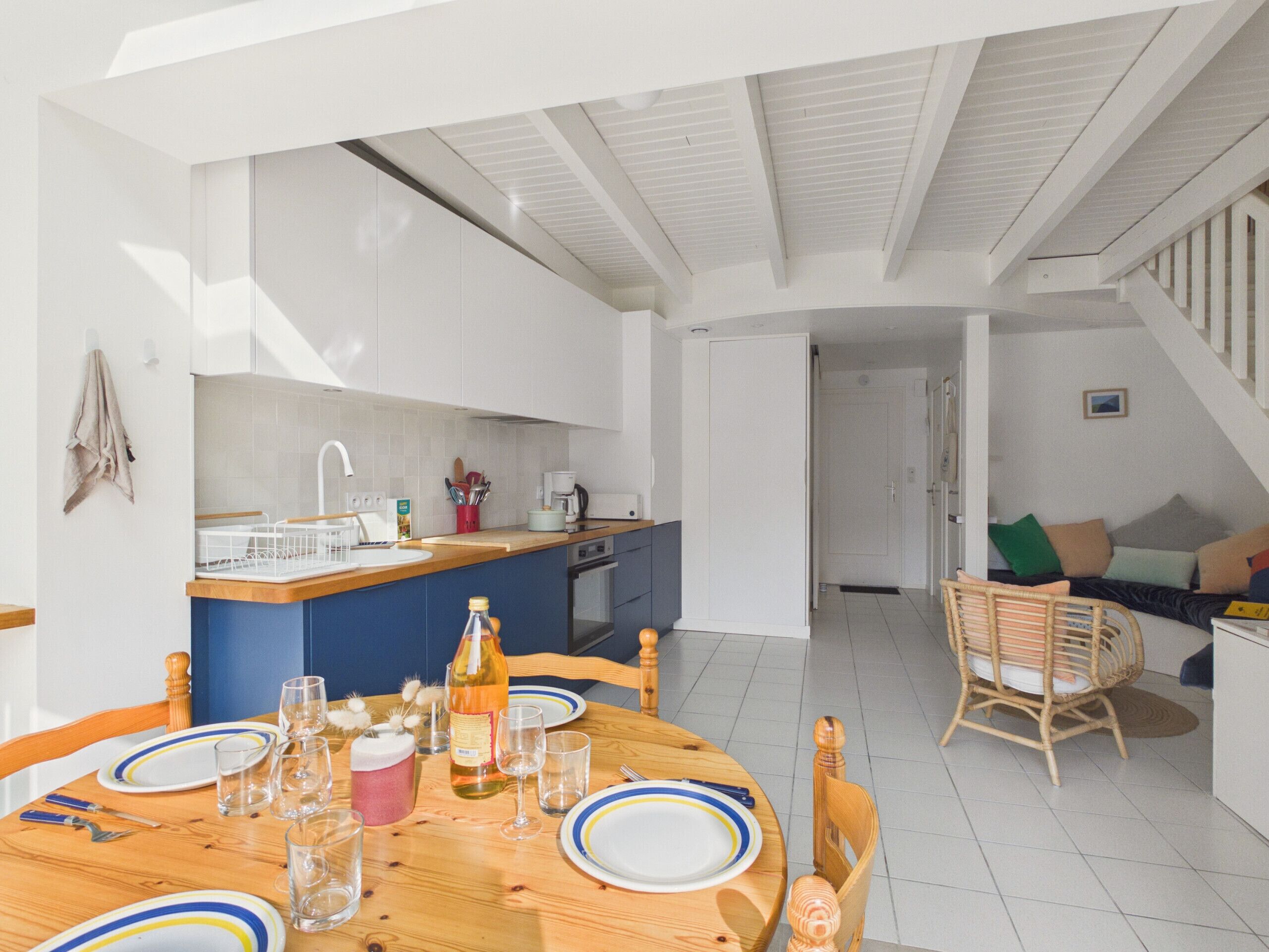 A modern kitchen with a central island, a dining area with a wooden table set for six, and a living area with a sofa and chairs.