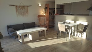 A living room with a sofa, a dining table with chairs, a kitchen area with cabinets, and a wall-mounted macrame decoration. - Cottage 200 m from Lac des Settons (Montsauche-les-Settons)