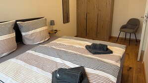 Een slaapkamer met een bed, twee kussens, een nachtkastje, een lamp, een kledingkast en een stoel.