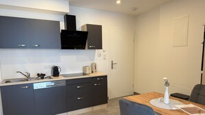 Een moderne keuken met grijze kastjes, een ingebouwde magnetron en een eethoek met een houten tafel en stoelen.