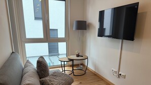 Een moderne woonkamer met een bank, een klein rond tafeltje, een lamp en een tv aan de muur.