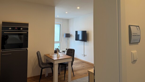 Een moderne keuken met een oven, een eettafel met stoelen, een flatscreen televisie aan de muur en een bord met de locatie erop.