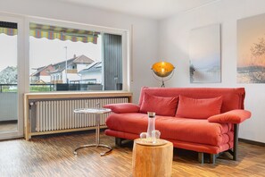 A modern living room with a red sofa, a small round table, a floor lamp, and a radiator. - Studio G11 – Exclusive Apartment with Private Spa, Balcony & Parking (Uhldingen-Mühlhofen)