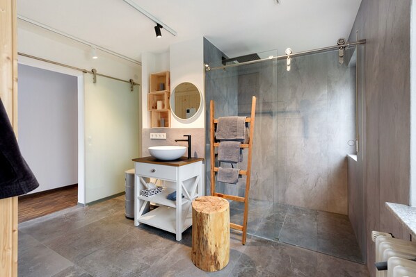 A modern bathroom with a large mirror, wooden vanity, and a glass shower enclosure.