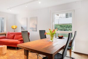 A modern living room with a wooden dining table, red sofa, and black chairs. - Studio G11 – Exclusive Apartment with Private Spa, Balcony & Parking (Uhldingen-Mühlhofen)
