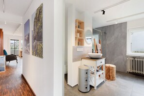 Ein modernes Badezimmer mit einem großen Spiegel, einem Waschbecken und einem hölzernen Hocker.