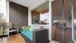 Ein Balkon mit einer Rattan-Couch, einem Sessel und einer Schiebetür zu einer Küchenzeile.