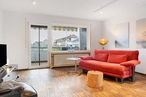 A modern living room with a red sofa, a wooden coffee table, a TV, and a radiator. - Studio G11 – Exclusive Apartment with Private Spa, Balcony & Parking (Uhldingen-Mühlhofen)