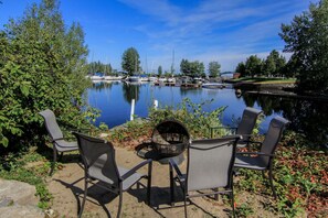 Une terrasse au bord du lac, dotée de chaises et d’un foyer, qui offre une vue sur une marina remplie de bateaux.