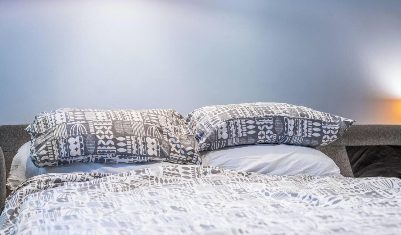 A bed with patterned bedding and pillows, a headboard, and a view of the sky.