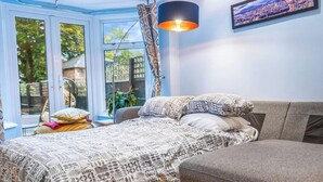 Quarto com cama, sofá, pintura de paisagem urbana e janela com cortinas.
