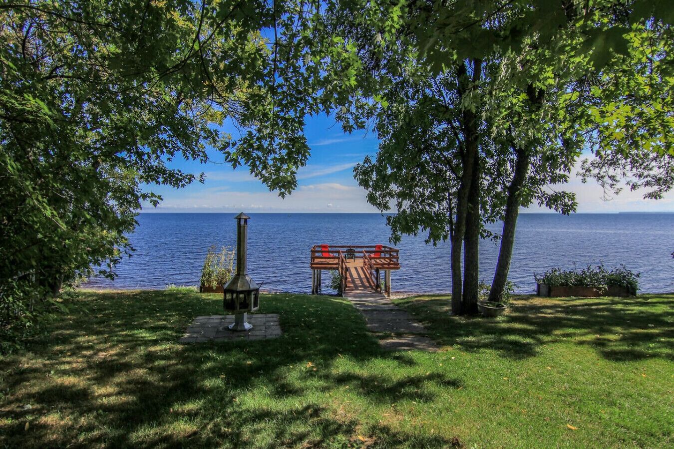 A lakeside deck with a grill and seating area, surrounded by trees and overlooking the water.