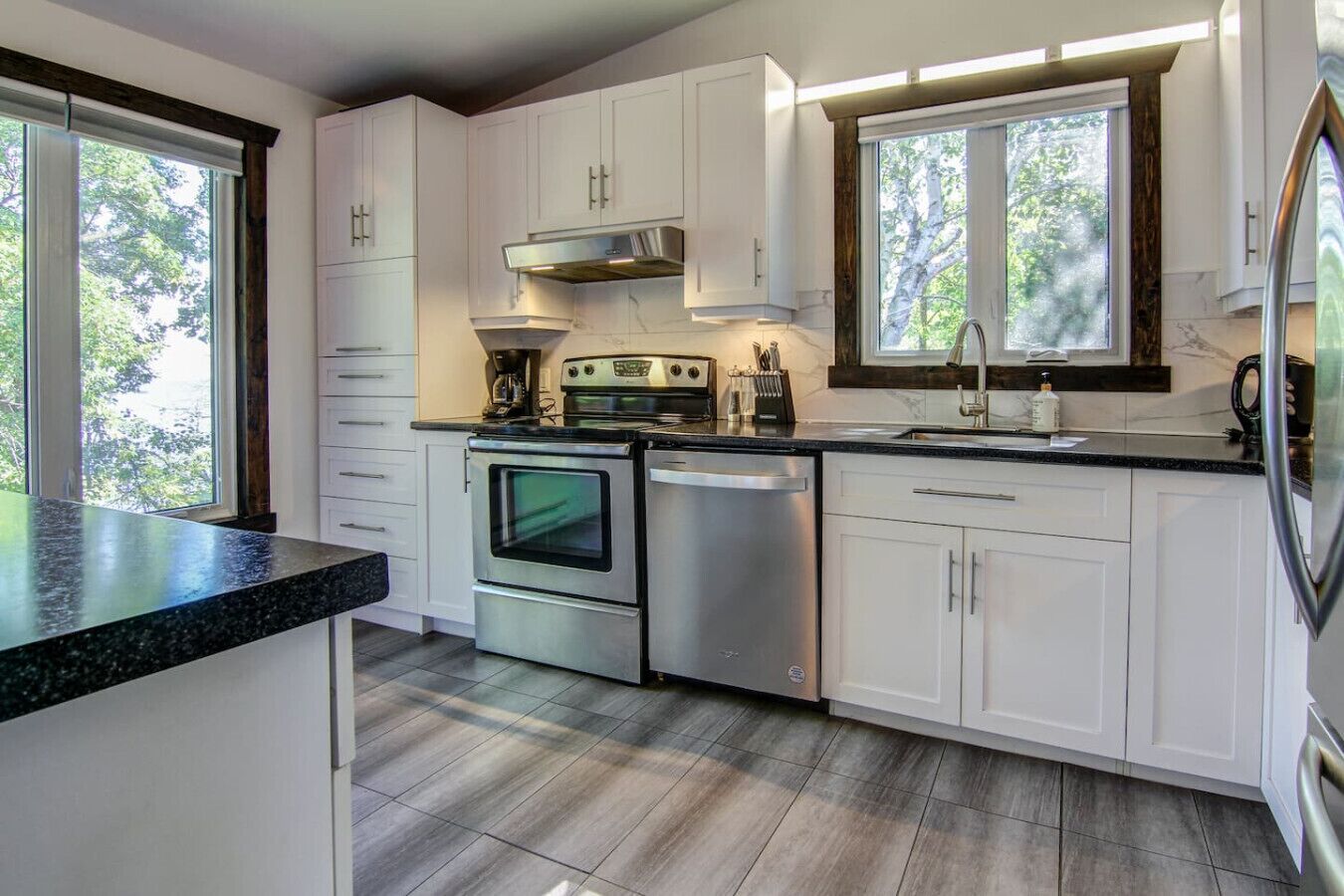 A modern kitchen with white cabinetry, stainless steel appliances, and a large window providing natural light.