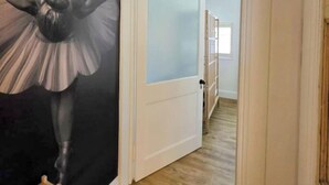 Un pasillo con un amplio mural floral a la izquierda, una puerta blanca con vidrio satinado y suelo de madera.
