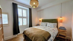 Un dormitorio con cama, cortinas, lámpara colgante y mesita de noche.